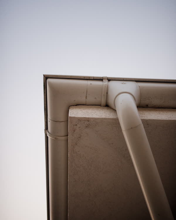 White gutter turning a corner under the eaves, with its downspout running down the wall